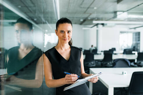 A front view of young businesswoman with clipboard in an office, standing. - HPIF18052