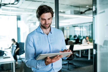 Ein Porträt eines jungen Geschäftsmannes mit Tablet, der in einem Büro steht und arbeitet. - HPIF18057