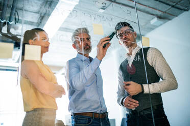 Frontalansicht einer Gruppe von Geschäftsleuten, die in einem Büro stehen und ein Brainstorming durchführen, aufgenommen durch Glas. - HPIF18059