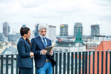 A mature businessman and young businesswoman with diary standing outdoors on a terrace, working. - HPIF18070