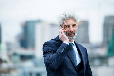 A portrait of mature businessman with smartphone standing on a terrace, working. - HPIF18076