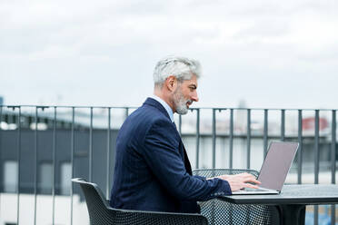 A mature businessman with laptop sitting at the table on a terrace, working. - HPIF18081