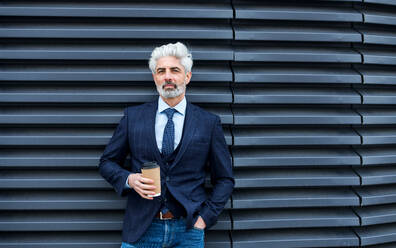 A mature businessman standing outdoors, holding paper cup with coffee. Copy space. - HPIF18089