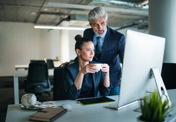 Zwei Geschäftsleute mit einem Computer stehen in einem Büro am Schreibtisch und arbeiten. - HPIF18097