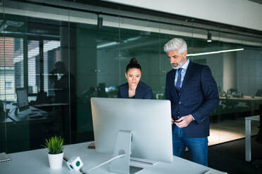 Zwei Geschäftsleute mit Computer in einem Büro stehen am Schreibtisch und arbeiten. - HPIF18100