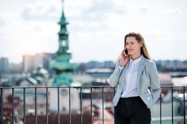 A young businesswoman with smartphone standing on a terrace, making a phone call. - HPIF18133