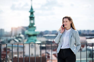 Eine junge Geschäftsfrau mit Smartphone steht auf einer Terrasse und führt ein Telefongespräch. - HPIF18133