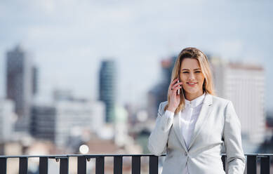 A young businesswoman with smartphone standing on a terrace, making a phone call. - HPIF18136