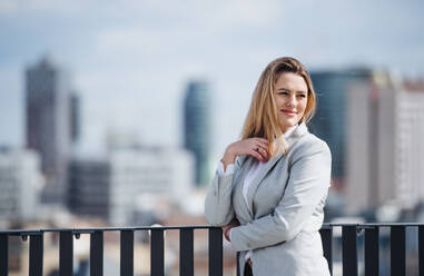 Ein Porträt einer jungen blonden Geschäftsfrau, die auf der Terrasse vor ihrem Büro steht. Kopierraum. - HPIF18139