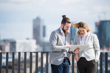 Zwei fröhliche junge Geschäftsleute mit Tablet stehen auf einer Terrasse vor einem Büro und arbeiten. - HPIF18144