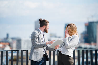 Zwei fröhliche junge Geschäftsleute mit Tablet stehen auf einer Terrasse vor einem Büro und arbeiten. - HPIF18147