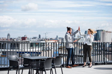 Zwei junge Geschäftsleute mit Tablet stehen auf einer Terrasse vor ihrem Büro und drücken ihre Begeisterung aus. - HPIF18148