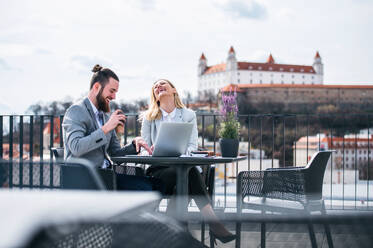 Zwei fröhliche junge Geschäftsleute mit Laptop sitzen auf einer Terrasse vor dem Büro und lachen bei der Arbeit. - HPIF18150