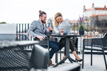 Zwei fröhliche junge Geschäftsleute mit Laptop sitzen auf einer Terrasse vor einem Büro in Bratislava und arbeiten. - HPIF18151