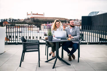 Zwei fröhliche junge Geschäftsleute mit Laptop sitzen auf einer Terrasse vor dem Büro und arbeiten. - HPIF18154