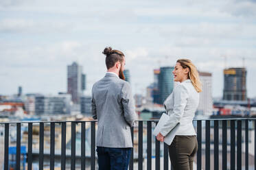 Two cheerful young business people with tablet standing on a terrace outside office, talking. - HPIF18170