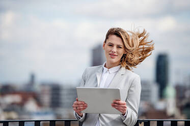 Vorderansicht einer jungen Geschäftsfrau mit Tablet, die auf einer Terrasse steht und in die Kamera schaut. - HPIF18177