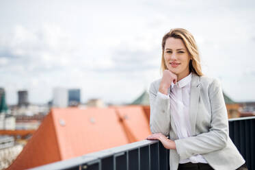 Ein Porträt einer jungen blonden Geschäftsfrau, die auf der Terrasse vor ihrem Büro steht. Kopierraum. - HPIF18180