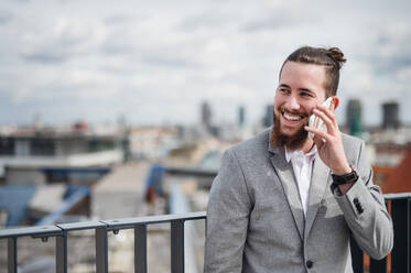 A young businessman with smartphone standing on a terrace outside office, making a phone call. - HPIF18182