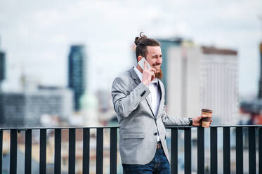 Ein junger Geschäftsmann mit Smartphone steht auf einer Terrasse vor seinem Büro und führt ein Telefongespräch. - HPIF18186