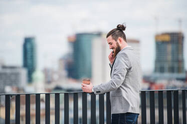 Ein junger Geschäftsmann mit Smartphone steht auf einer Terrasse vor seinem Büro und führt ein Telefongespräch. - HPIF18187