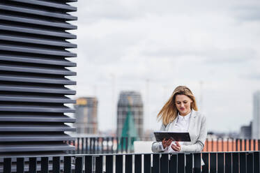 Eine junge, glückliche Geschäftsfrau mit Tablet, die auf einer Terrasse steht und arbeitet. - HPIF18199