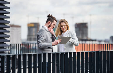 Zwei fröhliche junge Geschäftsleute mit Tablet stehen auf einer Terrasse vor einem Büro und arbeiten. - HPIF18202