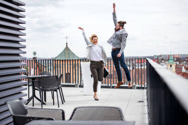 Zwei junge Geschäftsleute, die auf einer Terrasse vor ihrem Büro springen und ihre Begeisterung zum Ausdruck bringen. - HPIF18209