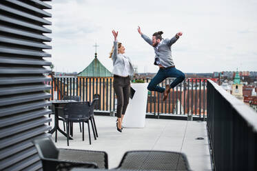 Zwei junge Geschäftsleute mit Tablet stehen auf einer Terrasse vor ihrem Büro und drücken ihre Begeisterung aus. - HPIF18210