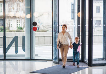 Eine Geschäftsfrau mit ihrer kleinen Tochter betritt ein Bürogebäude, geht spazieren und hält die Hände. - HPIF18214