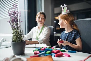 Eine Geschäftsfrau mit einer kleinen Tochter sitzt in einem Büro und arbeitet. - HPIF18225