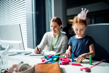 Eine Geschäftsfrau mit einer kleinen Tochter sitzt in einem Büro und arbeitet. - HPIF18227