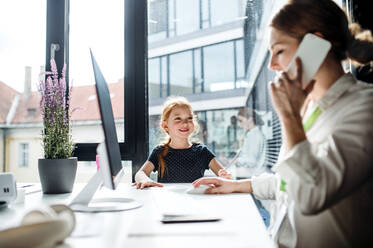 Eine Geschäftsfrau mit einer kleinen Tochter sitzt in einem Büro und arbeitet. - HPIF18234