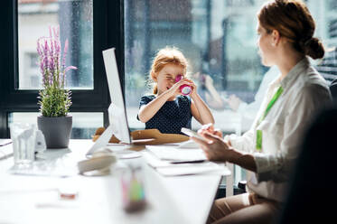 Eine Geschäftsfrau mit einer kleinen Tochter sitzt in einem Büro, arbeitet und spielt. - HPIF18235