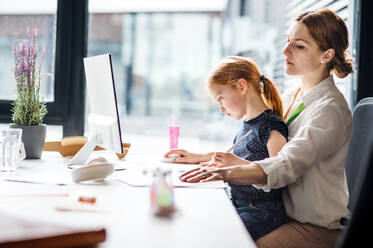 Eine Geschäftsfrau mit einer kleinen Tochter sitzt in einem Büro und arbeitet. - HPIF18236
