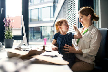 Eine Geschäftsfrau mit einer kleinen Tochter sitzt in einem Büro, arbeitet und spielt. - HPIF18240