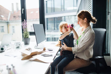 Eine Geschäftsfrau mit einer kleinen Tochter sitzt in einem Büro und arbeitet. - HPIF18242