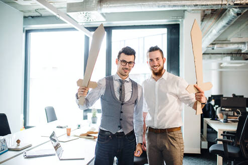 Two young businessmen with cardboard swords in an office. A competition concept. - HPIF18250