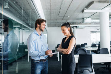 Young businesspeople with clipboard standing in an office, working. - HPIF18281