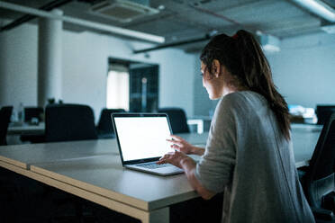 Rückansicht einer jungen Geschäftsfrau mit Computer, die in einem Büro sitzt und arbeitet. - HPIF18294