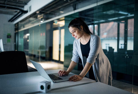 Seitenansicht einer jungen Geschäftsfrau mit Computer, die in einem Büro am Schreibtisch steht und arbeitet. - HPIF18296