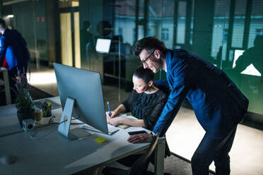 Zwei Geschäftsleute mit einem Computer sitzen in einem Büro am Schreibtisch und arbeiten. - HPIF18299