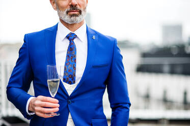 A midsection of mature businessman with champagne in glass having a party outdoors on roof terrace in city. - HPIF18324