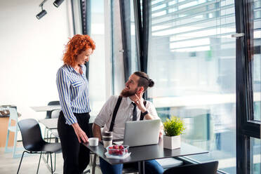 Two cheerful businesspeople in an office, using laptop. - HPIF18326