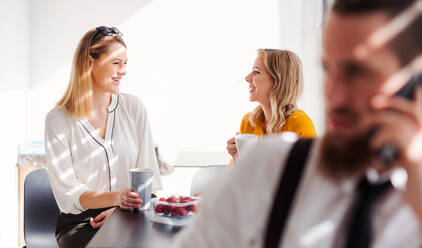 Junge, fröhliche Geschäftsfrauen in der Kaffeepause in der Büroküche, die sich unterhalten. - HPIF18328