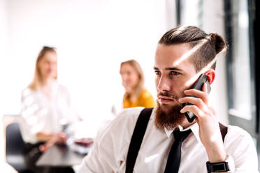 Ein Porträt eines jungen Geschäftsmannes mit Smartphone in einem Büro, der einen Anruf tätigt. - HPIF18329