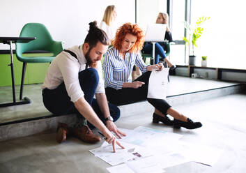 Two business people looking at paper documents on the floor in an office, talking. - HPIF18347