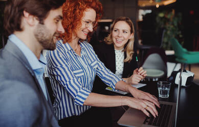 Eine Gruppe junger, fröhlicher Geschäftsleute mit Laptop sitzt in einem Büro und unterhält sich. - HPIF18359