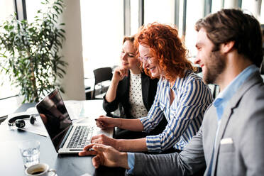 Eine Gruppe junger, fröhlicher Geschäftsleute mit Laptop sitzt in einem Büro und unterhält sich. - HPIF18360