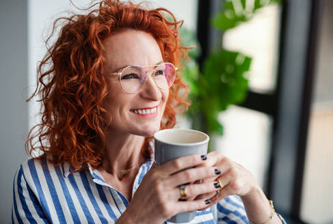 Ein Porträt einer glücklichen Geschäftsfrau in einem Büro, die eine Tasse Kaffee in der Hand hält. - HPIF18398